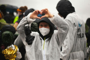  A person in the typical Ende Gelände action suit makes a heart with his fingers.