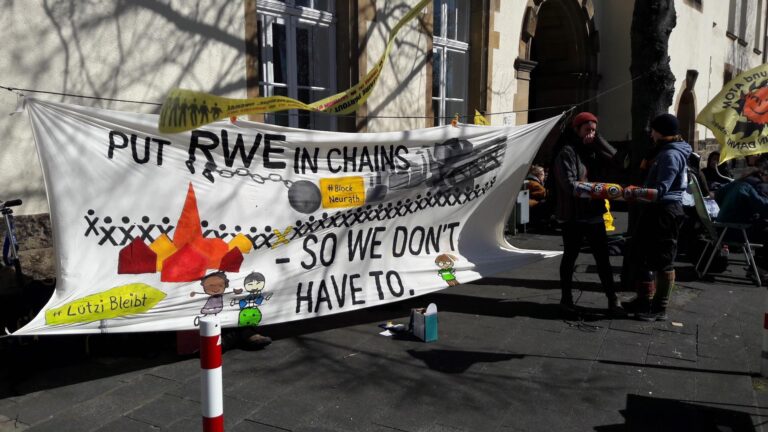 Vor dem Gericht stehen solidarische Menschen und halten ein Banner.