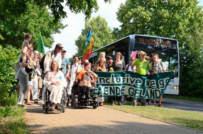 Auf dem Bild ist ein bunter Demonstrationszug von vorne abgebildet. Auf dem Foto sind ca. 15 Menschen, zwei davon im Rollstuhl. - The picture shows a colourful demonstration procession from the front. There are about 15 people in the photo, two of them in wheelchairs.